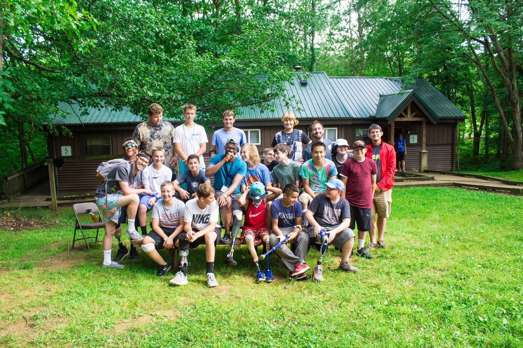 Ty and a large group of campers, including several with prosthetic legs, pose outside a cabin at camp