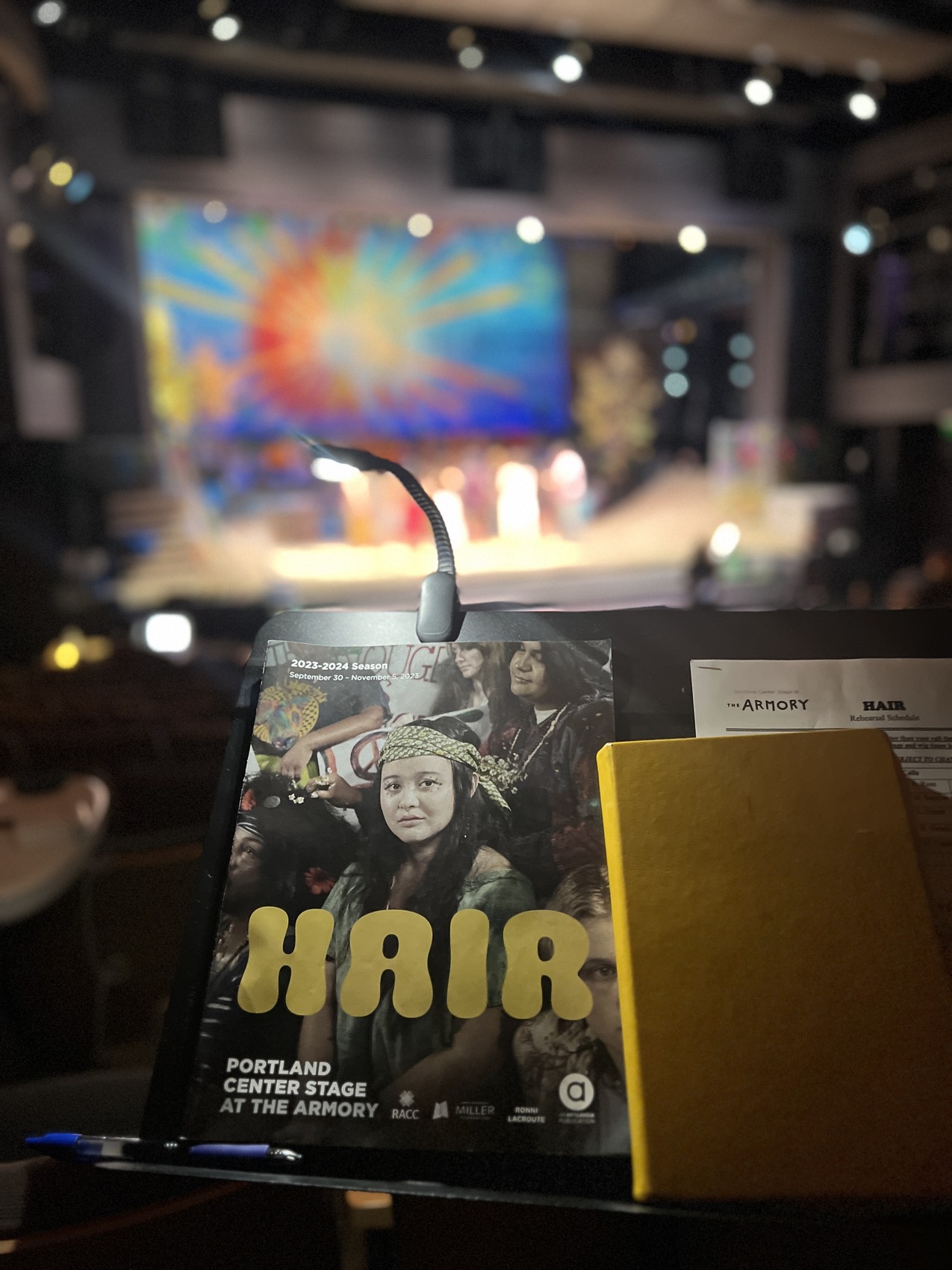 Music stand with the Hair program at Portland Center Stage, with the set visible on stage behind it